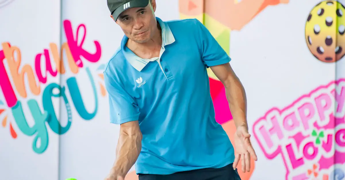 A man in a blue polo shirt and black cap plays pickleball outdoors, holding a paddle and hitting a ball, with colorful "Thank You" and "Happy Love" signs in the background.
