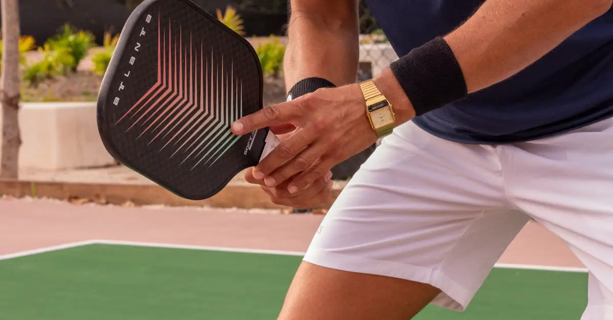 A person wearing a gold wristwatch and wristband holds a pickleball paddle, preparing to play on an outdoor court.