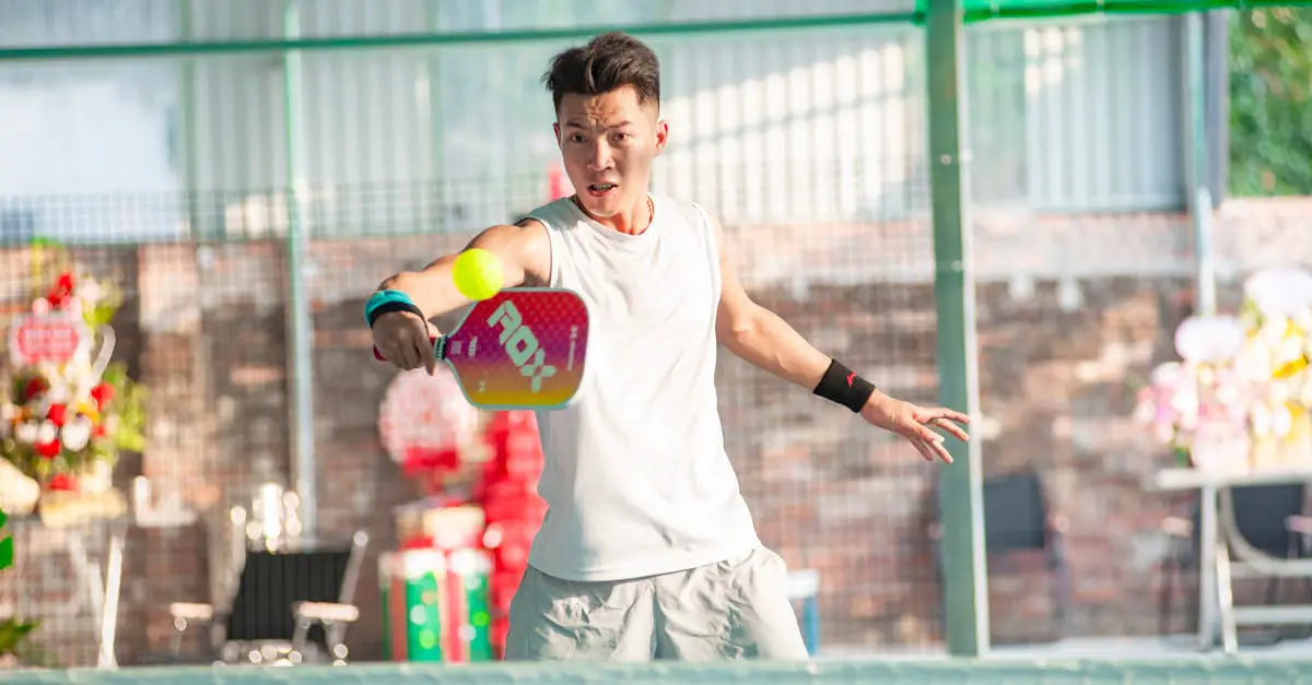 A man in athletic wear hits a yellow ball with a paddle on a pickleball court indoors.
