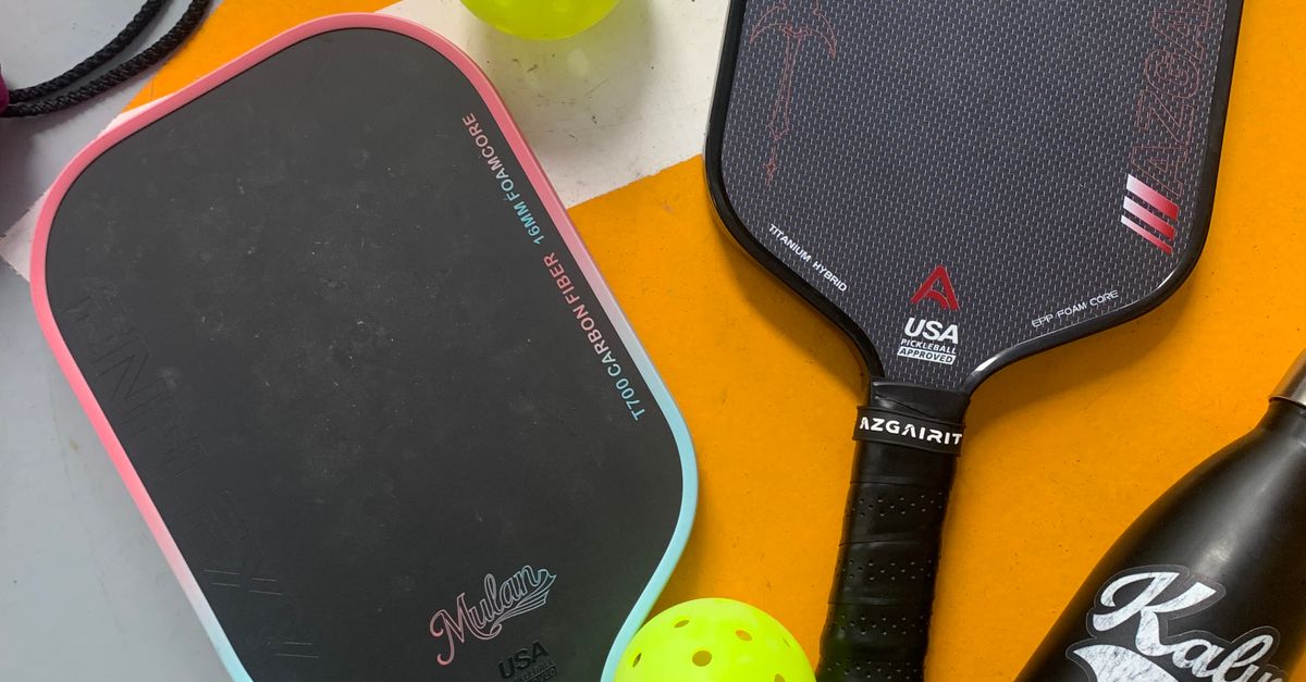 Two pickleball paddles, two yellow pickleballs, and a black water bottle are arranged on an orange and white surface.